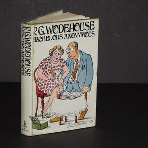 Può includere: Un libro vintage con copertina rigida intitolato "Bachelors Anonymous" di P.G. Wodehouse. La copertina presenta un'illustrazione colorata di un uomo e una donna, con il titolo in grassetto. Anche il dorso del libro mostra il titolo.