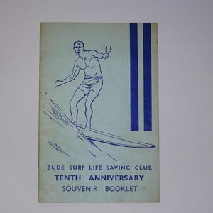 Może przedstawiać: Niebieska i biała broszura z rysunkiem osoby surfującej. Broszura nosi tytuł "Bude Surf Life Saving Club Dziesięciolecie Souvenir Booklet".