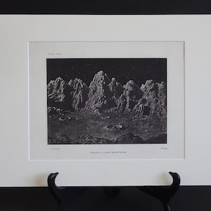 以下が含まれることがあります： 「GROUP II LOWER MOUNTAINS」と題された、クレーターのある山脈の白黒プリント。白いマットとフレームに入っており、黒いスタンドに飾られています。ヴィンテージイラストです。