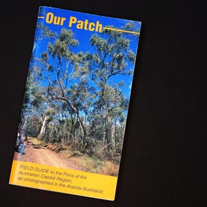 May include: A field guide titled "Our Patch" with a blue cover featuring a photograph of a forest with tall trees and a dirt path. The guide is for the flora of the Australian Capital Region, as photographed in the Aranda Bushland.