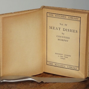 以下が含まれることがあります： 「The Kitchen Library」というタイトルの開かれた本で、副題は「Meat Dishes」で、著者はカウンテス・モルフィ。出版元はハーバート・ジョセフ、4 アダム・ストリート、アデルフィです。