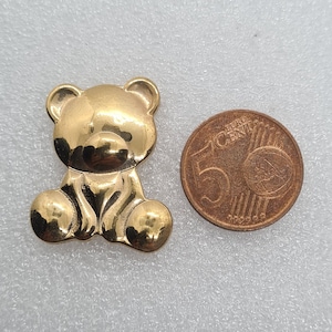 Könnte beinhalten: Ein goldfarbener Teddybär-Anhänger mit glatter, glänzender Oberfläche. Der Anhänger ist etwa so groß wie eine 5-Cent-Euro-Münze.