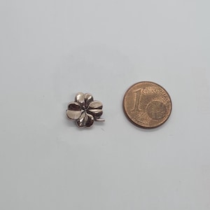 Può includere: Un ciondolo a forma di quadrifoglio in argento, mostrato accanto a una moneta da 1 centesimo di euro per il confronto delle dimensioni.