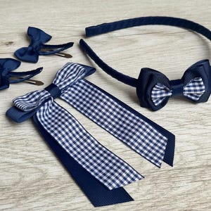 May include: A selection of navy blue and white hair accessories. The set includes two bow barrettes, a headband with a bow, and a large bow with long ribbons. The bows have a gingham pattern and solid navy blue.