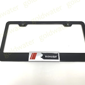 May include: Black license plate frame with a silver Roush Performance logo. The logo has a red accent stripe.