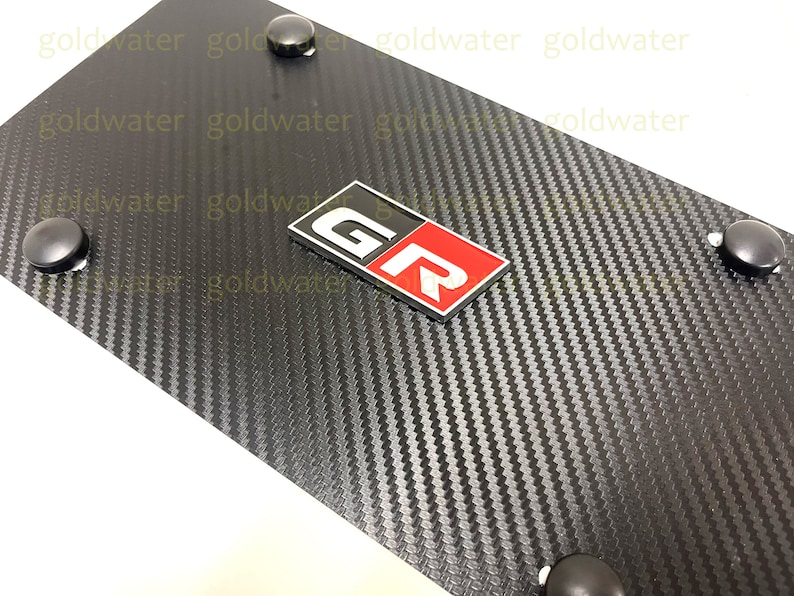 May include: Black carbon fibre license plate frame with a silver and red "GR" emblem.