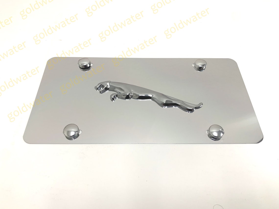May include: A silver metal license plate frame with a chrome jaguar logo in the center. The frame has four silver screw caps on the edges.