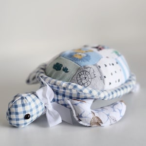 May include: A blue and white gingham fabric turtle toy with a white bow. The turtle's shell is made of patchwork fabric with various animal prints.