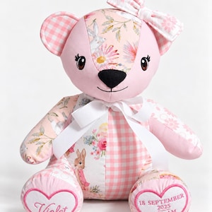 May include: A plush teddy bear made of pink fabric with a white gingham pattern and floral panels featuring rabbits. A white ribbon is tied around the neck. The left foot has the name Violet, and the right foot displays 18 SEPTEMBER 2025, 3:42 AM, 3:28 KG.