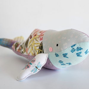 May include: A patchwork whale plush toy with a floral pattern, blue butterflies, and a pink nose. The whale is made of soft fabric and has a whimsical design.