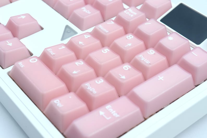 May include: Close-up of a computer keyboard's numeric keypad with light pink keycaps. The keys are labeled with white numbers, symbols, and functions. The keyboard has a white frame.