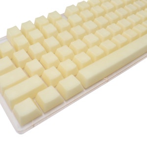 May include: A close-up of a keyboard with light yellow keycaps. The keycaps are arranged in a standard layout, with a long space bar and smaller keys. The keyboard is set against a white background.