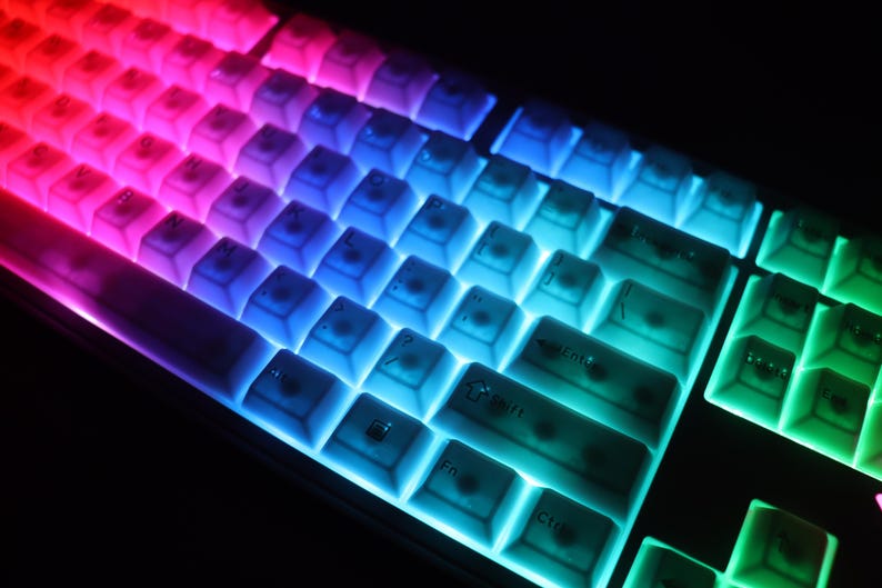 May include: Close-up of a backlit computer keyboard with a gradient of colors. The keys transition from red to purple, blue, and green. The keyboard is illuminated, creating a vibrant and colorful display.