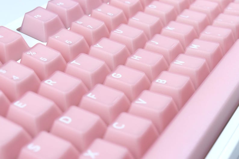 May include: Close-up of a pink mechanical keyboard with white lettering on the keys. The keys are a soft, pastel pink color. The keyboard is angled, showing the keys in rows.