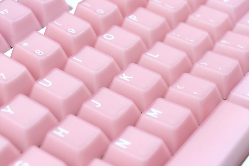 May include: Close-up of a computer keyboard with light pink keycaps. The keys are arranged in rows and columns, with white lettering and symbols. The keyboard has a clean, modern aesthetic.