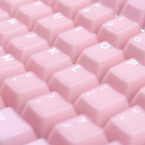 May include: Close-up of a pink keyboard with white lettering. The keys are a soft, pastel pink color and arranged in a standard QWERTY layout. The letters and symbols are in white.