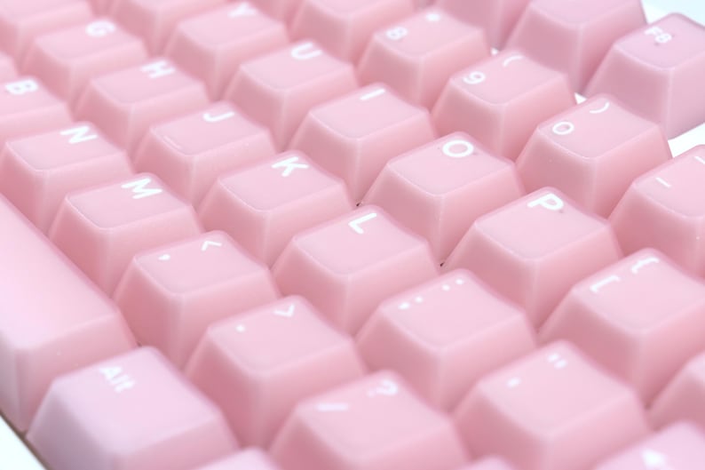 May include: Close-up of a pink keyboard with white lettering. The keys are a soft, pastel pink color and arranged in a standard QWERTY layout. The letters and symbols are in white.