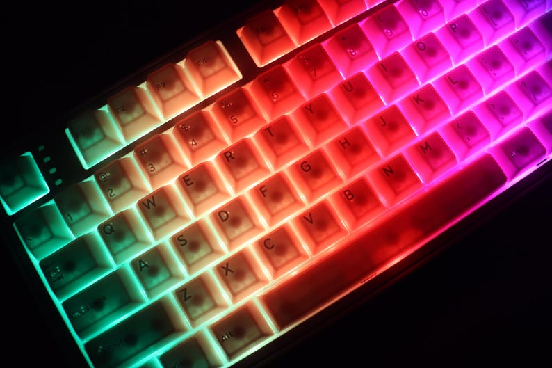 May include: A close-up of a mechanical keyboard with illuminated keys. The keys are lit with a gradient of colors, transitioning from green to red to purple. The keyboard has a standard QWERTY layout.