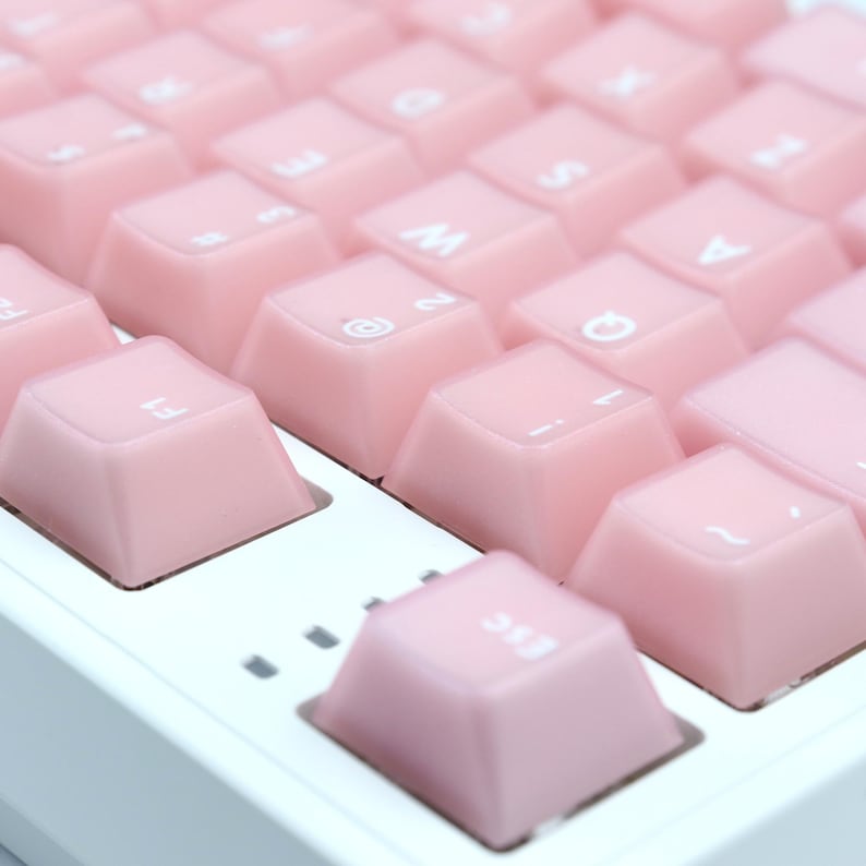 May include: Close-up of a mechanical keyboard with light pink keycaps. The keys are arranged in a grid pattern, with white lettering visible on some keys. The keyboard has a white base and a minimalist design.