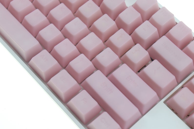 K&ouml;nnte beinhalten: Nahaufnahme einer mechanischen Tastatur mit hellrosa Tastenkappen. Die Tasten sind in einem Standard-Layout angeordnet, mit gr&ouml;&szlig;eren Tasten f&uuml;r Leertaste und Shift. Die Tastatur hat einen wei&szlig;en Rahmen.