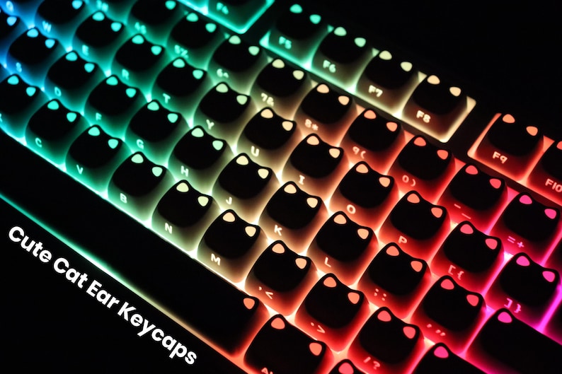 May include: Close-up of a keyboard with black keycaps shaped like cat ears. The keys are backlit with a gradient of colors, transitioning from blue to green, yellow, orange, and red. The text "Cute Cat Ear Keycaps" is visible.