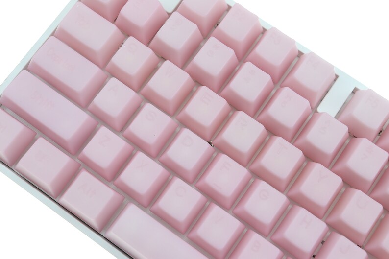 K&ouml;nnte beinhalten: Nahaufnahme einer kompakten Tastatur mit hellrosa Tastenkappen. Die Tasten sind in einem Raster angeordnet, mit einem wei&szlig;en Rahmen. Die Tastatur hat ein minimalistisches Design.