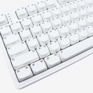 May include: A white mechanical keyboard with custom keycaps. The keycaps are white with gray accents and a unique design. The keyboard has a standard layout with function keys and a number pad.