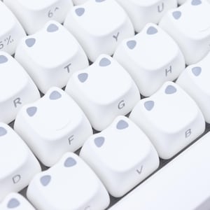 May include: Close-up of a white keyboard with custom keycaps. The keycaps are white with gray accents and feature a unique design. Letters and symbols are printed on the keys.
