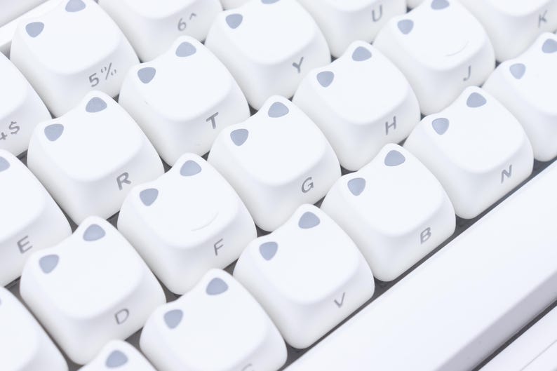 May include: Close-up of a white keyboard with custom keycaps. The keycaps are white with gray accents and feature a unique design. Letters and symbols are printed on the keys.
