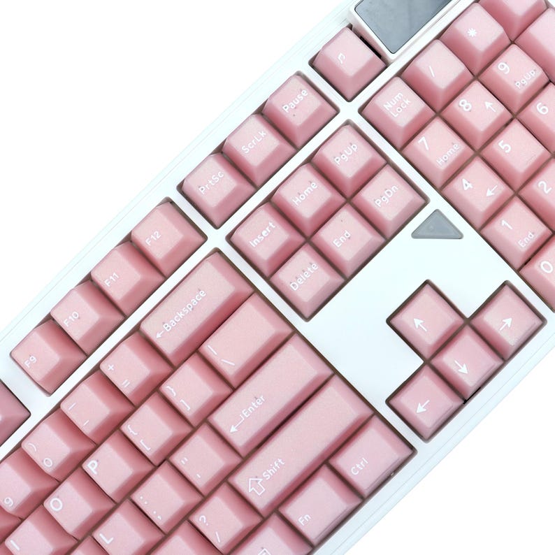 May include: A close-up of a white and pink mechanical keyboard. The keyboard has pink keycaps with white lettering and a white frame. The keys include function keys, number keys, and arrow keys.