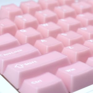 May include: Close-up of a computer keyboard with light pink keycaps. The keys are arranged in rows and columns, with white lettering. The Shift, CapsLock, Ctrl, and Win keys are visible. The keyboard has a clean, minimalist design.
