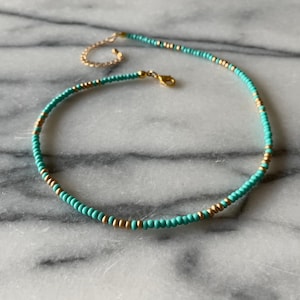 May include: A turquoise and gold beaded choker necklace with a gold clasp.