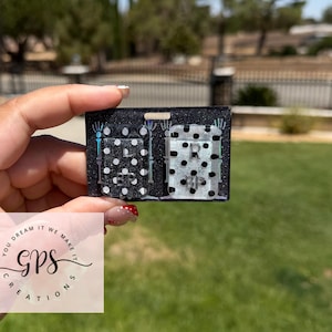 May include: A rectangular black glitter badge reel featuring two white rectangular inserts with black polka dots. The left insert is marked with the letter L and the letters BP, while the right insert is marked with the letter R and the letters BP.