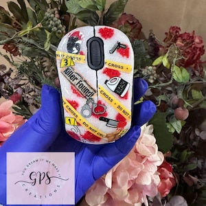 May include: A white computer mouse with a glossy finish featuring red splatter patterns, yellow crime scene tape with the text "DO NOT CROSS" and "Killer Found", and small illustrations of a handgun, handcuffs, a bleach bottle, and a knife.