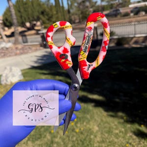 May include: Scissors with red and white patterned handles, featuring the text "Killer Found" and "Do Not Cross". The scissors are held in a gloved hand, with a logo that reads "GPS Creations".