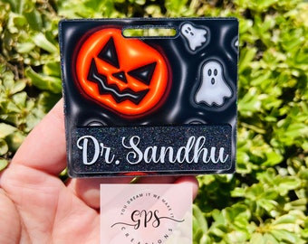 May include: A black and orange Halloween-themed name tag with a jack-o'-lantern and ghosts. The name tag says "Dr. Sandhu" in white text.