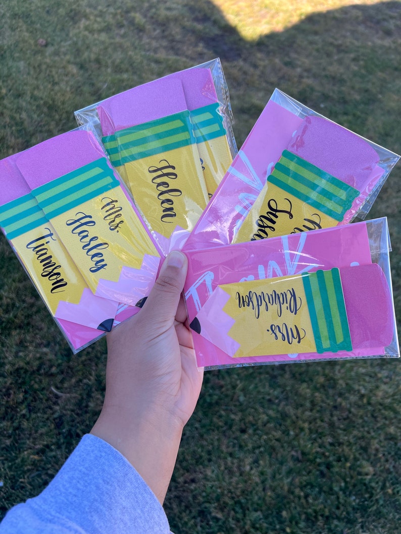 Pu&ograve; includere: Quattro etichette regalo a forma di matita rosa e gialla con strisce verdi. Le etichette sono etichettate con i nomi "Miss Tiamson", "Miss Haslem", "Helen" e "Mrs. Richardson".