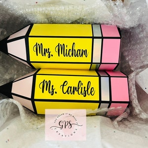 May include: Two yellow pencil-shaped boxes with pink and black accents. The boxes are decorated with the names "Mrs. Micham" and "Ms. Carlisle".