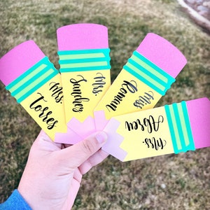 Pu&ograve; includere: Cinque carte gialle a forma di matita con gomme rosa e strisce verdi. Ogni carta ha il nome di un insegnante scritto in corsivo nero: "Miss Torres", "Miss Sanchez", "Miss Bowman", "Miss Ogden" e "Miss Green".