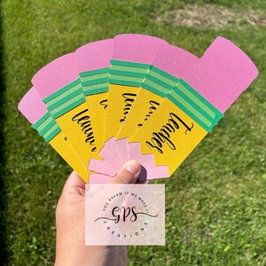 Pu&ograve; includere: Un set di sei segnalibri a forma di matita rosa e gialla con strisce verdi e la parola "Teacher" scritta su ogni segnalibro. I segnalibri sono tenuti in una mano. L'immagine include anche un logo per "GPS Creations" nella parte inferiore centrale dell'immagine.