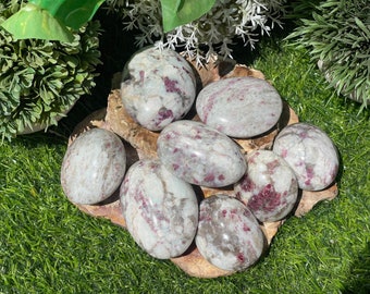 May include: A collection of eight tumbled stones with a white and pink color scheme. The stones have a smooth, polished surface and are arranged on a wooden surface.