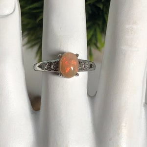 May include: A silver ring with a light brown oval opal gemstone and small clear stones on the band.