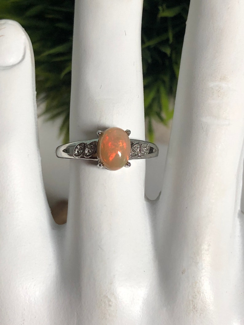 May include: A silver ring with a light brown oval opal gemstone and small clear stones on the band.