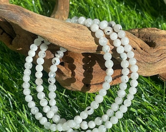 May include: A white and black gemstone bracelet with round beads. The bracelet is made of natural stones and is wrapped around a piece of driftwood.