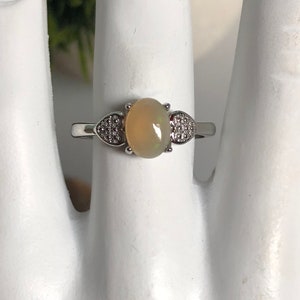 May include: A silver ring with a light brown oval opal gemstone and two heart-shaped accents set with smaller clear stones.