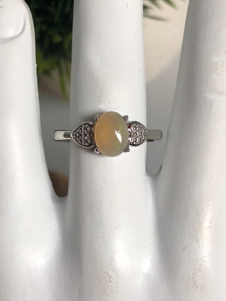 May include: A silver ring with a light brown oval opal gemstone and two heart-shaped accents set with smaller clear stones.
