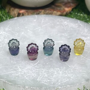 May include: Five small glass figurines in the shape of flowers with different colored glass. The flowers are arranged in a row on a white surface.