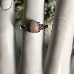 May include: A silver ring with a white opal gemstone set in a delicate, floral design. The ring is accented with small, clear stones.