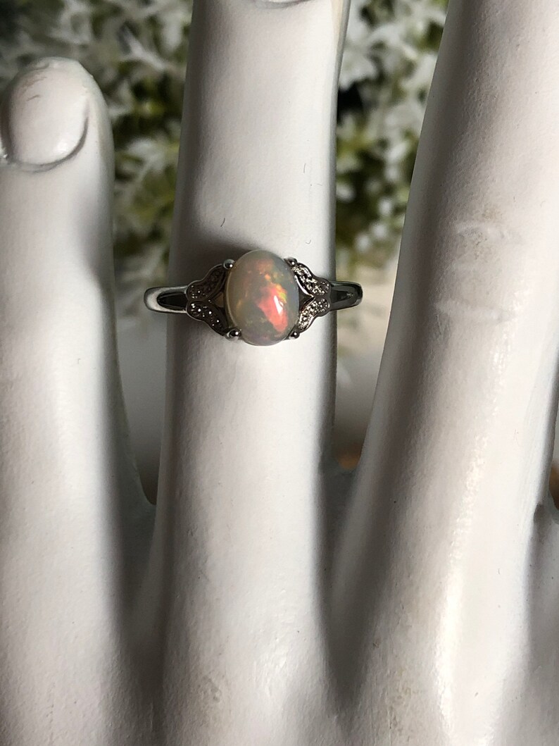 May include: A silver ring with a white opal gemstone set in a delicate, floral design. The ring is accented with small, clear stones.