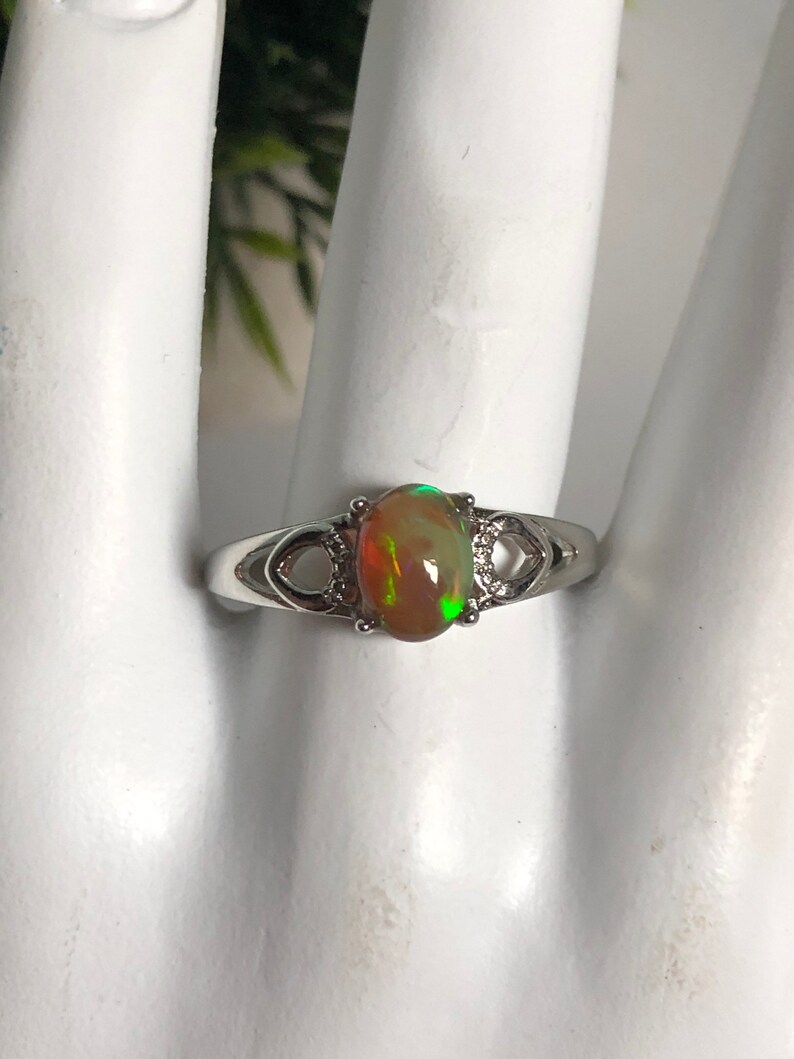May include: A silver ring with an oval-shaped opal gemstone. The opal has a green, orange, and red iridescent sheen.